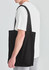 A black canvas tote bag is worn over the shoulder by a person in a white t-shirt and grey sweatpants.