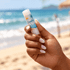 A hand holding a white tube of Twist Lip Balm with a beach and ocean background. The product features a logo.