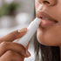 A twist lip balm in a white container being applied to lips. The person has light skin and natural-looking makeup.