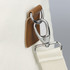 A close-up of a cream tote bag featuring a silver clip attachment and a brown leather detail.