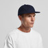 A navy wool cap with a flat brim, worn by a model in a white shirt. The cap features a logo.