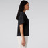 A black boxy tee displayed on a model from the side, featuring a simple design and an unembellished appearance.