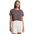 A model wearing a dark grey cropped t-shirt paired with light-coloured shorts. The shirt has a logo.