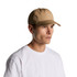 A tan cap worn by a man with short hair, featuring a structured design and a logo.