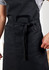 A black apron featuring a waist tie and front pockets, designed for practical workwear use.