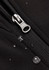 A close-up of a black soft shell jacket featuring a zipper and droplets of water on the fabric.