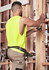 A sleeveless high-visibility yellow tee worn by a man working on a construction site, measuring with a tool.