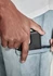 A close-up of a hand placing a phone into the pocket of light blue stretch jeans. The jeans feature a subtle logo.