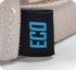 A close-up of a beige cap featuring a small black tag with a blue logo, indicating it is eco-friendly.