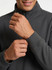 A man adjusts the cuff of a grey half zip fleece jumper featuring a high collar and a logo.