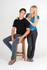 A black women's V-neck T-shirt displayed on a model, paired with blue jeans, alongside a seated male model.