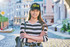 A cap in black with tear drop perforations, worn by a smiling young woman with long hair, standing in a street setting.