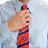 A person adjusting a red tie featuring blue patterns, worn over a light blue shirt. The tie has a logo.