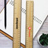Two bamboo rulers, one with a logo, placed on a notebook with a pen and a small plant nearby.