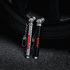 Two key chain tyre gauges, one silver and one black, attached to a keyring, positioned near a tyre.