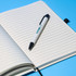 An A5 lined notebook in cream colour with a black pen resting on the pages, set against a blue background.