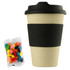 A reusable 12oz bamboo coffee cup in cream with a black sleeve, accompanied by a bag of colourful jelly beans.