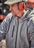 A man wearing a grey unisex packable rain jacket, with ear protection, outdoors in a work environment.