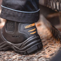 WorkTough Mens Dealer Work Safety Steel Toe Midsole Ankle Boots, close-up of black safety boots with orange accents on rugged textured ground for industrial safety footwear.