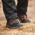 Scruffs Air Mens S3 Safety Bungee Lace Lightweight Composite Trainers, close-up of black and orange safety trainers on sandy ground with black work pants.