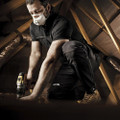 Scruffs Pro Flex Plus Holster Mens Codura Stretch Workwear Trousers, a man wearing black work trousers with a logo, working in an attic with a drill, wearing a face mask and work boots.