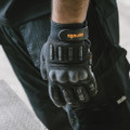 Scruffs Trade Shock Impact Mens Work Padded Palm Gloves, close-up of black protective gloves with padded palms and grip-enhancing ridges, worn by a person for industrial or construction work.