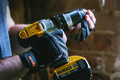 Scruffs Trade Precision Men's Work Padded Palm Gloves, close-up of a person wearing black and gray work gloves while holding power tools.