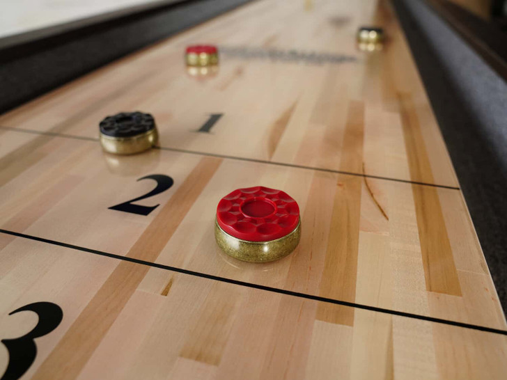 Close-up of the Portland Shuffleboard Table’s maple playfield, showing detailed scoring zones with red and black pucks in action. The butcher-block surface and protective polymer coating are visible for smooth gameplay.