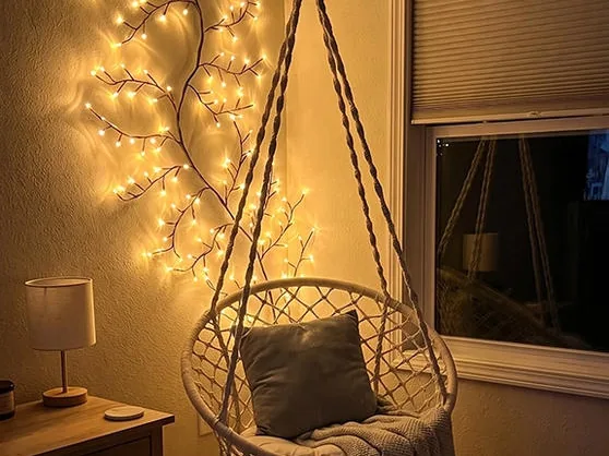 A lit vine light trailing across the wall behind a hanging macramé chair