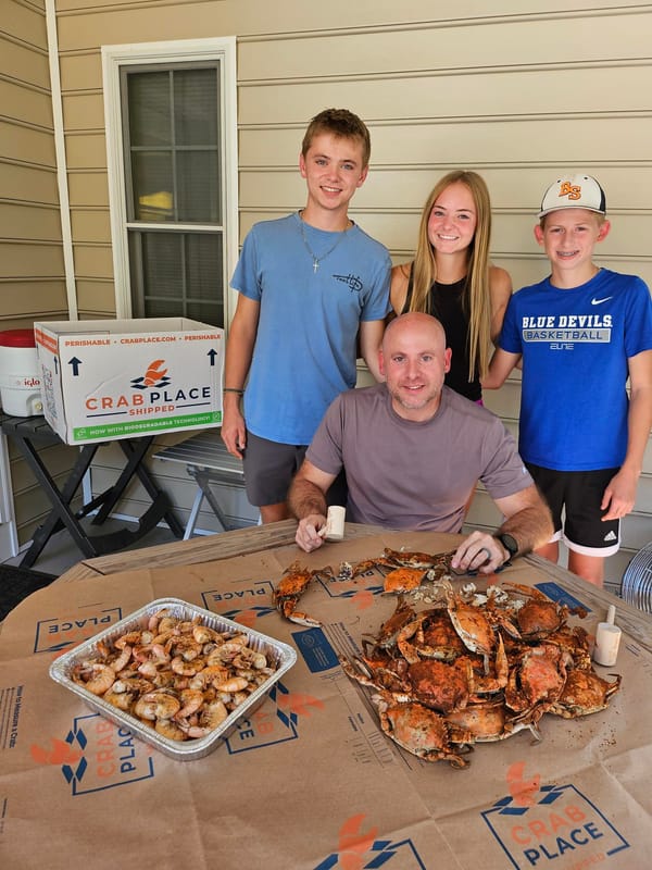 Family on the patio with a tray of steamed crabs and the Crab Place box
