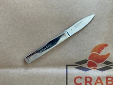 Stainless steel crab picking knife with Crab Knife stamped on the handle, lying on a box with a crab logo.