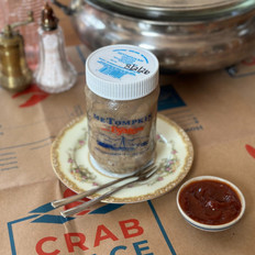 MetomPkin crab meat jar displayed on vintage plate with The Crab Place branded box, seafood cocktail sauce, and tableware in background.
