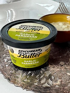 Tub of Epicurean Butter Garlic Parmesan flavored butter on a silver tray beside a small bowl of the butter and a fork.