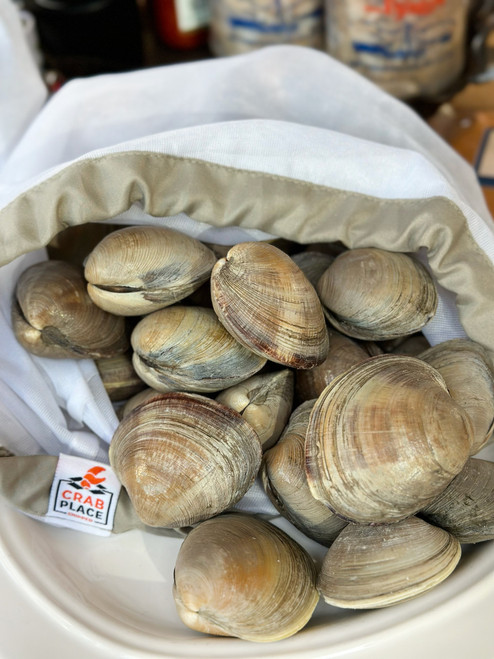 Whole clams in their shells nestled in white paper lined with branded The Crab Place label.