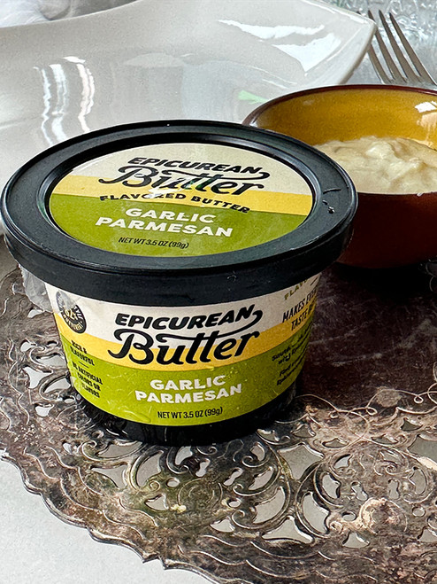 Tub of Epicurean Butter Garlic Parmesan flavored butter on a silver tray beside a small bowl of the butter and a fork.