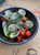 Steamed middleneck clams with red tomato chunks and lime wedge arranged in a black bowl.