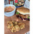 Fried oyster sandwich on a roll with breaded oysters and sauce in a white ramekin, styled overhead on a wooden surface.