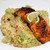 Blackened Alaskan king salmon fillet topped with lime slices over quinoa salad with cucumber and herbs on a white plate.
