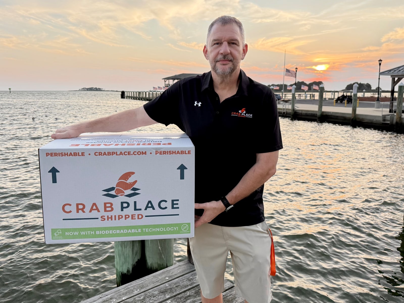 Greg Cain, founder of The Crab Place, holding a Crab Place shipping box on the dock in Crisfield, Maryland at sunset