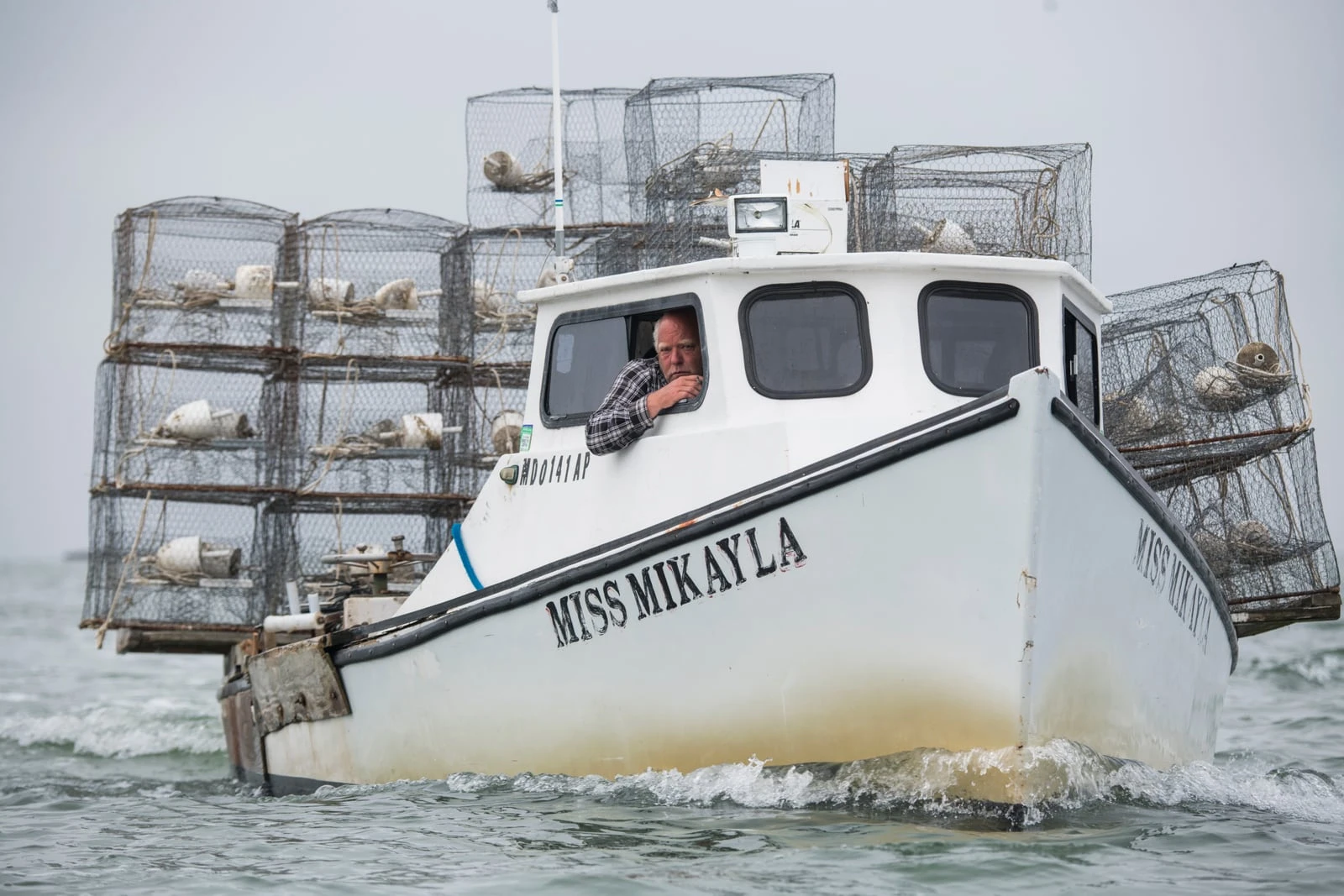 A Crab Place waterman at the helm of the Miss Mikayla, her deck stacked with crab pots on the Chesapeake Bay
