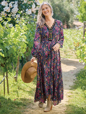 Image of woman walking through a floral path wearing the colorful Meena Maxi Dress