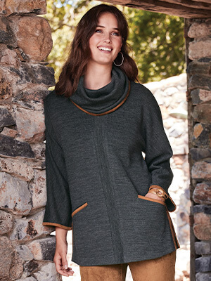 Image of a woman leaning against a stone wall wearing the gray Hanna Convertible Tunic with orange accents