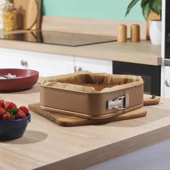 Gold square springform cake tin with baked cake, on kitchen worktop