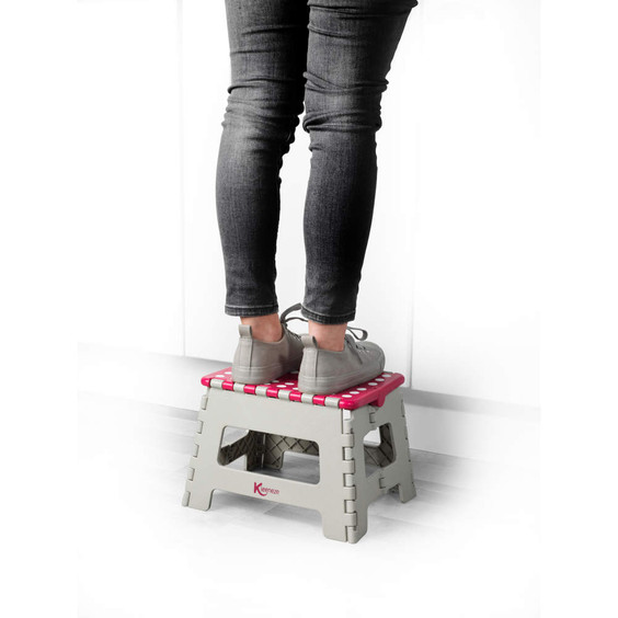 Foldable grey plastic step stool with pink polka dot top, shown in use.