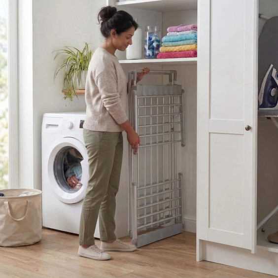 Foldable silver clothes airer in laundry area, being stored upright next to washing machine