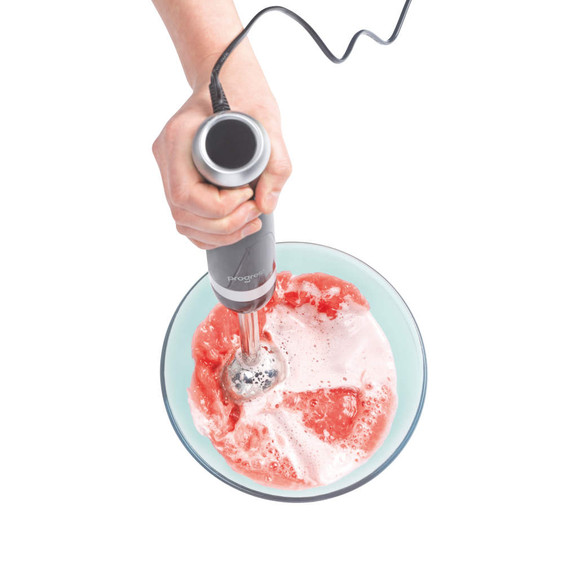 Hand blender mixing pink smoothie in glass bowl, close-up of Progress brand appliance.
