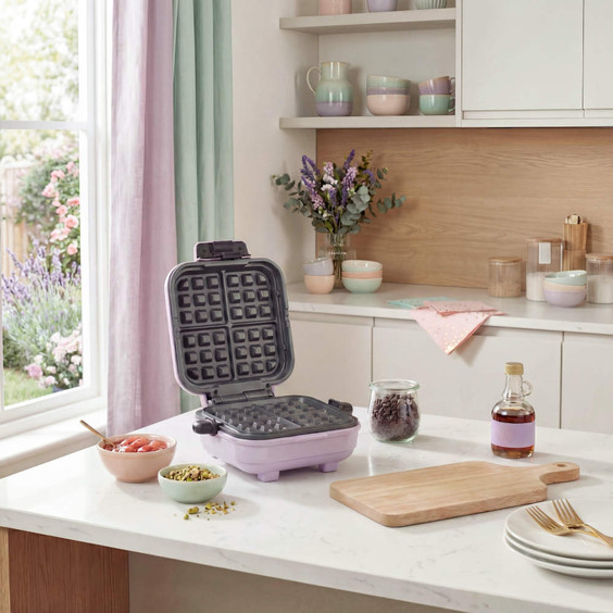 Purple waffle maker open on kitchen counter with ingredients and syrup bottle