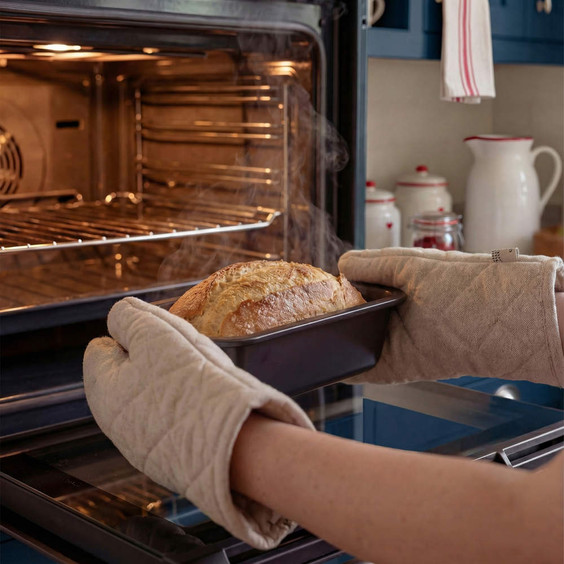 Removing freshly baked bread from oven using beige oven gloves