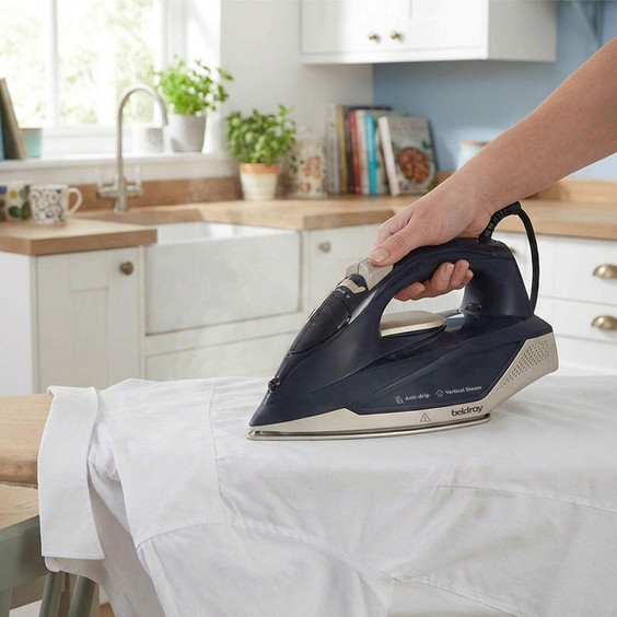 Navy steam iron pressing white shirt in modern kitchen, showing anti-drip feature.
