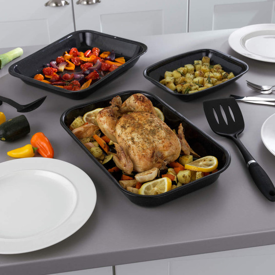 Set of three black roaster trays with chicken and vegetables on a kitchen worktop